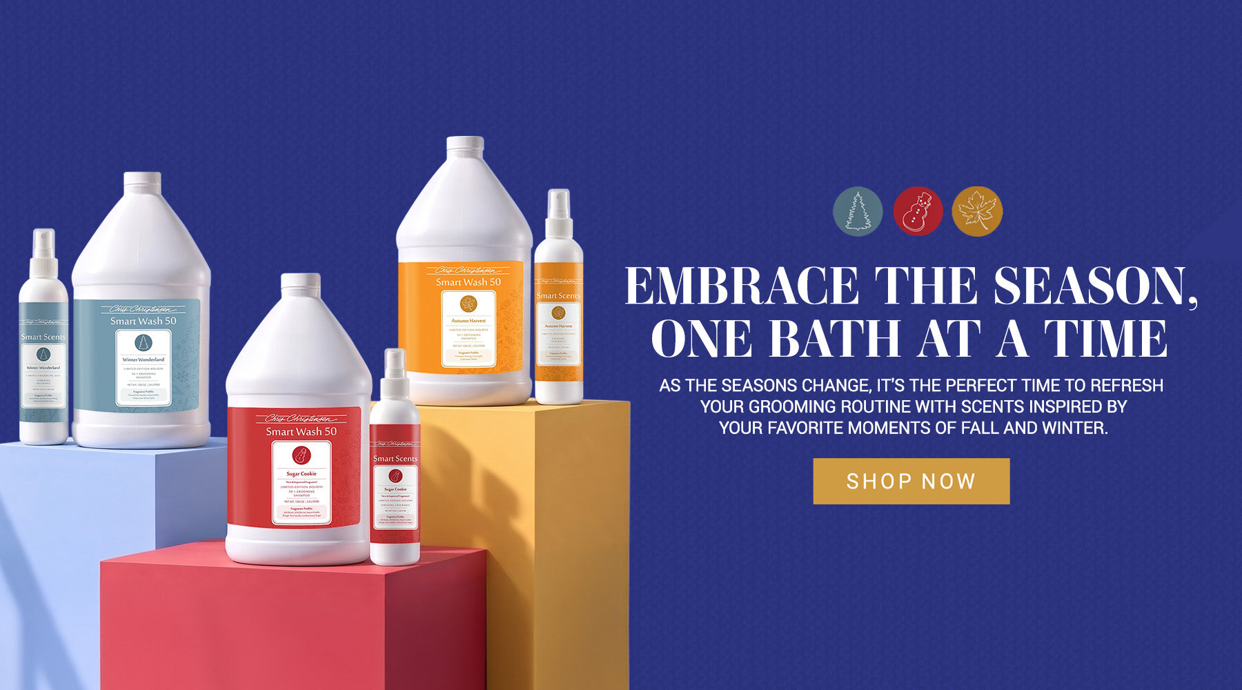 A promotional product display for Chris Christensen SmartWash Holiday scents on colorful pedestals against a deep blue background. Multiple white plastic bottles and a spray bottle with orange, red, and light blue labels are arranged on blue, yellow, and red blocks.